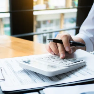 A person using the Standard calculator and holding a pen, works on documents at a wooden desk.